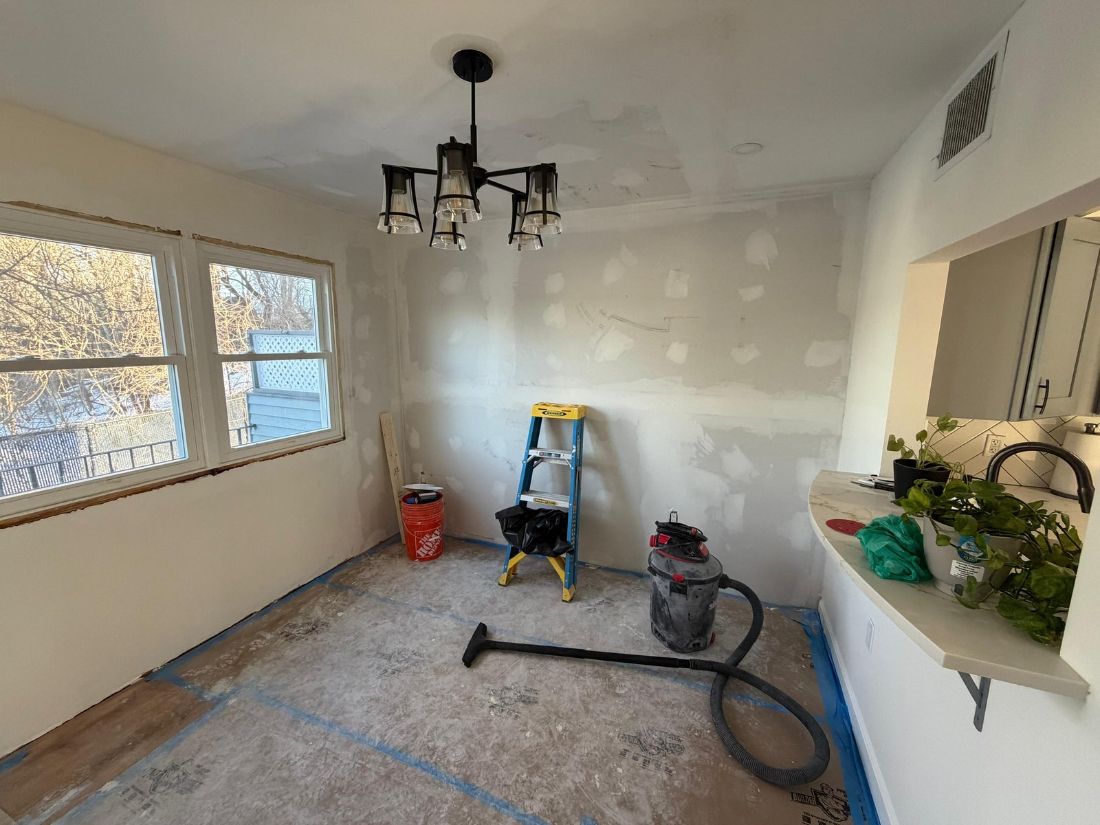 Dining area mid-restoration in West Roxbury MA showing new drywall mudded chandelier installed and floor protection in place — SR Enterprises